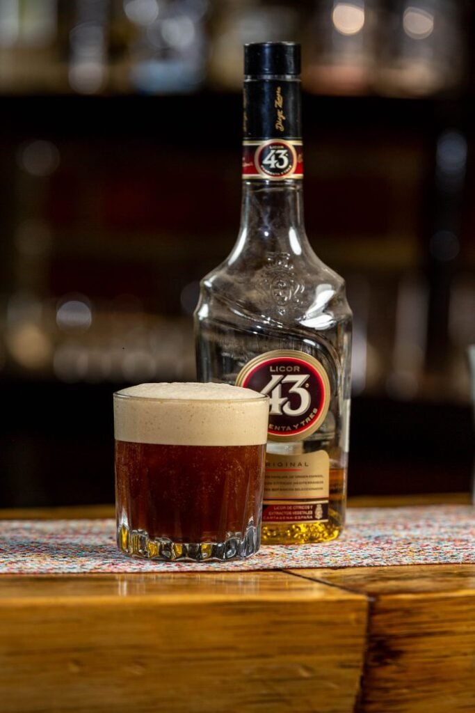 A bottle of Licor 43 and a cocktail glass on a bar counter inside a dimly lit bar.