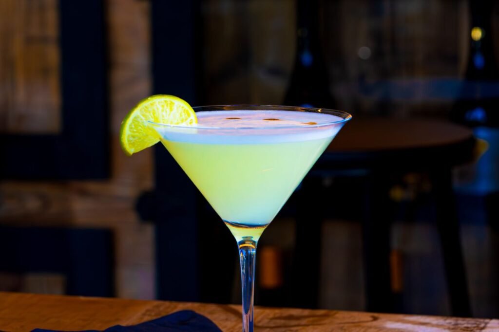 A vibrant lime martini in a glass with a lime wedge on a wooden bar.
