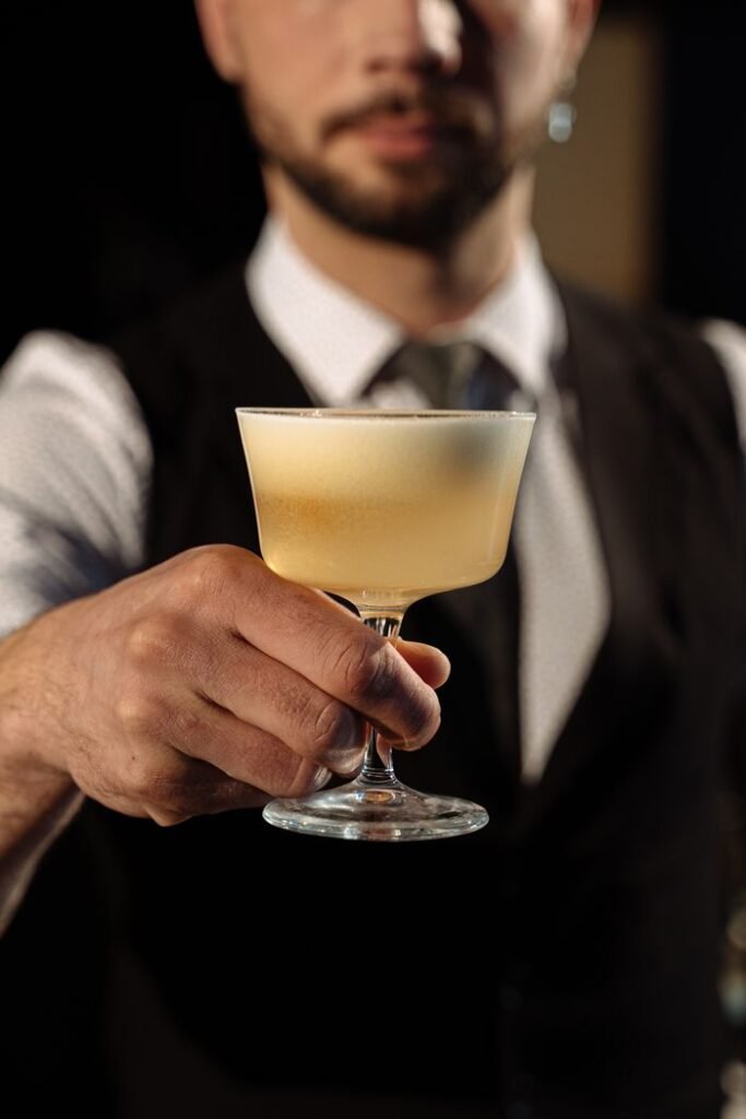 A professional bartender presenting a frothy cocktail in a stylish glass, perfect for promotional use.